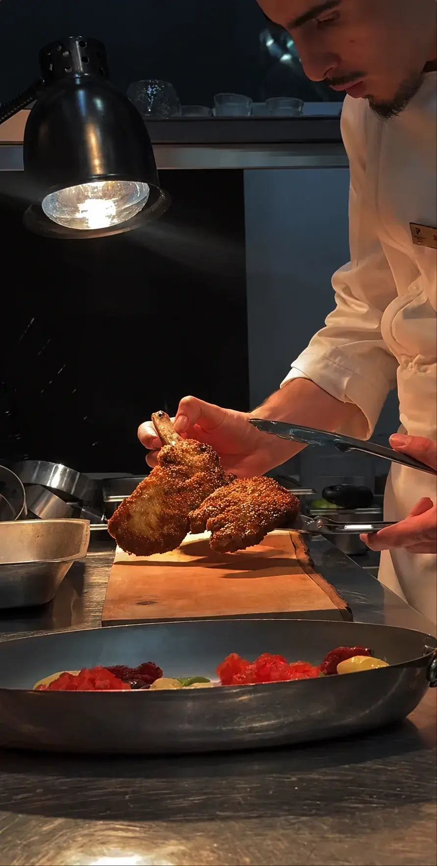 A chef carefully finishing a dish under the pass light